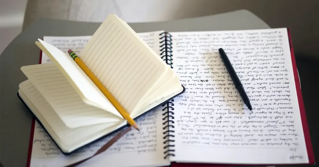手書きの文字で埋まったノートと、開いた手帳、鉛筆とペン